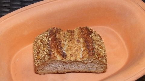 Ein Laib Brot liegt in einem flachen, erdigen Tonbehälter und sieht frisch aus, um länger frisch zu bleiben.