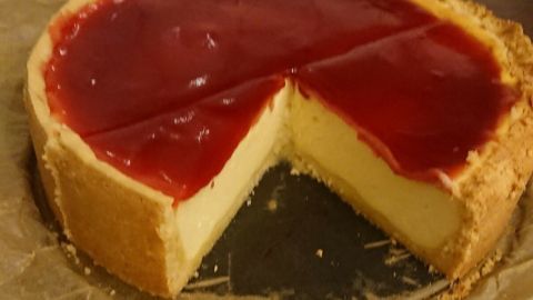 Ein Käsekuchen mit roter Gelee-Oberfläche steht auf einer Arbeitsplatte, ein Stück ist herausgeschnitten.