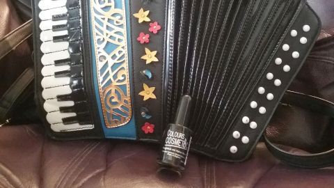 Kunstledertaschen mit abgestoßenen Ecken müssen nicht gleich entsorgt werden. Kostengünstig & schnell kann man die Ecken mit Nagellack kaschieren. Eine schwarze Kunstledertasche im Design eines Akkordeons liegt auf einem weichen, beigen Hintergrund.