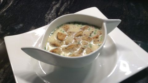 Eine cremige Knoblauchcremesuppe wird in einer eleganten Schüssel serviert, platziert auf einem weißen Teller.