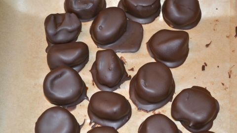 Süße Rumpflaumen-Pralinen liegen auf einem Blech, bereit zum Servieren in einem Frühstücksglas voller Pflaumen in Rum.
