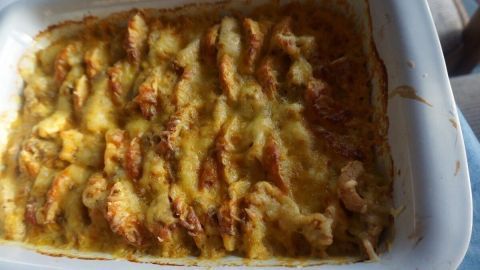Ein goldbrauner Apfel-Putenfleisch-Auflauf liegt in einer weißen Auflaufform auf einem Tisch, bereit zum Servieren.