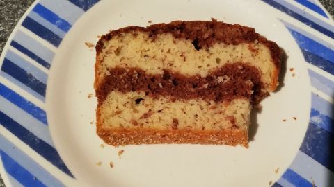 Ein Stück kalorienreduzierter Zebrakuchen liegt auf einem runden Teller mit blauen Streifen, auf einer grauen Arbeitsfläche.