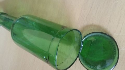 Eine grüne Glasflasche steht auf einem Tisch, ihr Boden liegt daneben. Das Bild zeigt den Prozess, den Flaschenboden herauszulösen.