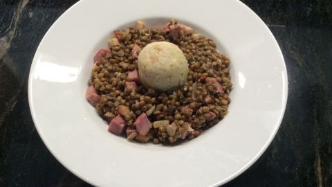 Eine Schüssel Linsen mit Rauchspeck und Selchfleischwürfeln, garniert mit einer Knödelportion in der Mitte.
