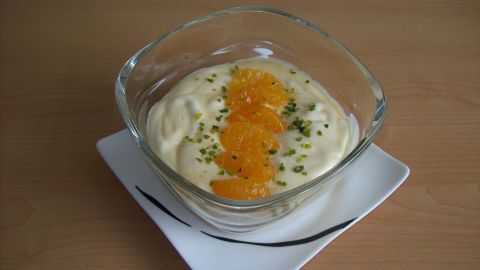 Ein Mandarinen-Sahne-Dessert in einer Schüssel mit orangefarbenen Mandarinenstücken und grünem Ziersel, serviert auf einem Teller.