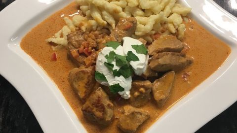 Ein herzhaftes Paprika-Rahm-Gulasch mit zarten Fleischstücken, serviert mit Spätzle auf einem eleganten Teller.