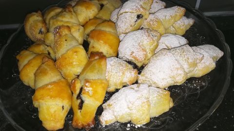 Frisch gebackene Schmalzkipferl liegen auf einer Glasplatte, einige mit Puderzucker bestäubt, bereit zum Servieren.