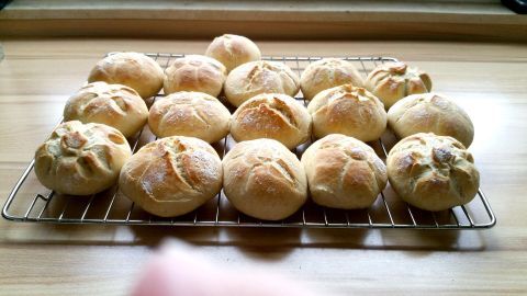 Auf einem Gitterrost liegen frisch gebackene, helle Knusperbrötchen, die appetitlich goldbraun und gleichmäßig gerundet sind.