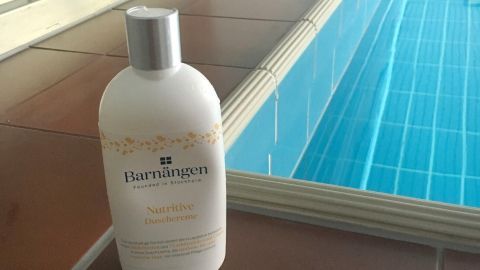 Eine Flasche Hautpflege steht am Rand eines Schwimmbads, bereit, sensible Haut nach dem Schwimmen zu pflegen.