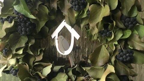 Ein Frühlingskranz aus grünen Blättern und blauen Beeren hängt an einem Haken vor einer glatten Oberfläche.