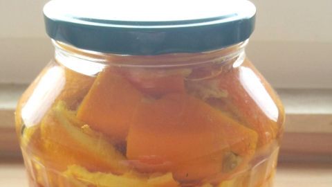 Ein Glas mit orangenen Orangenschalen befindet sich auf einem Holztisch und wird zur Herstellung von Entkalker und Reiniger genutzt.