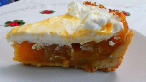 Ein Stück Karamellpudding-Kuchen mit Apfel, garniert mit Sahne, liegt auf einem weißen Teller in einer gemütlichen Umgebung.