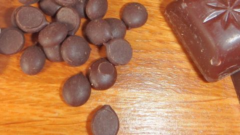 Dunkle Schokoladentaler liegen verstreut auf einem Holztisch, während eine Schokoladentafel daneben liegt.