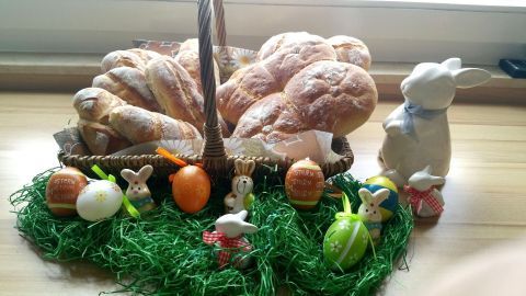 Frische Schmand-Brötchen liegen in einem Korb, umgeben von bunte Ostereiern und einem kleinen Hasen auf grünem Gras.
