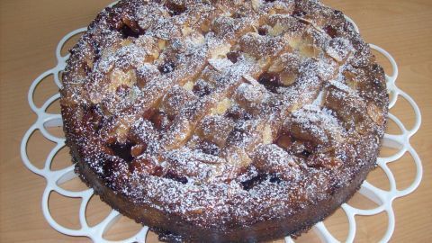 Eine Linzer Torte liegt auf einem dekorativen weißen Kuchenständer, mit Puderzucker bestäubt und in einer gemütlichen Umgebung.