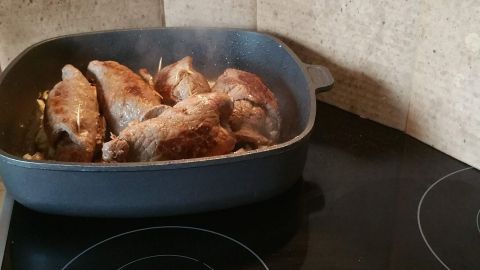 Ein Karton-Spritzschutz steht hinter einem Kochtopf mit Fleisch auf einem modernen Kochfeld in einer Küche.