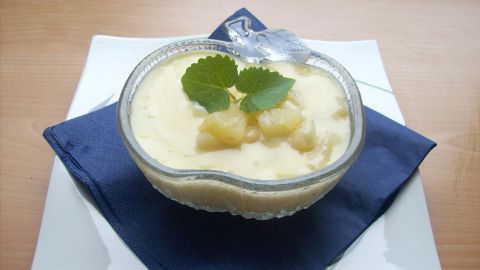 Eine Dessertschale mit Ananas-Vanille-Creme steht auf einem blauen Servietten, garniert mit frischen Minzblättern.