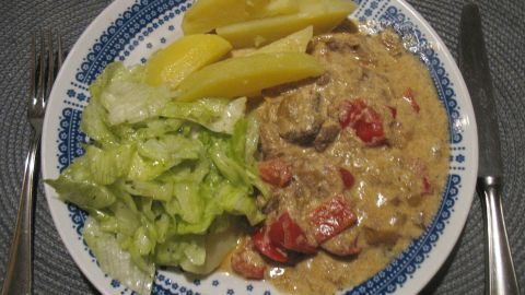 Hier das Paprika-Sahne-Gulasch mit Salzkartoffeln und frischem Salat auf einem Teller angerichtet.