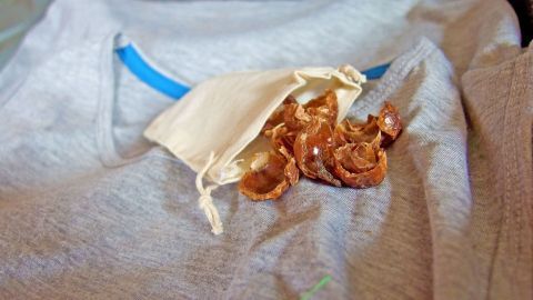 Waschnussschalen liegen lose aus einem kleinen Säckchen auf einem hellen T-Shirt, um die ökologische Verwendung zu zeigen.