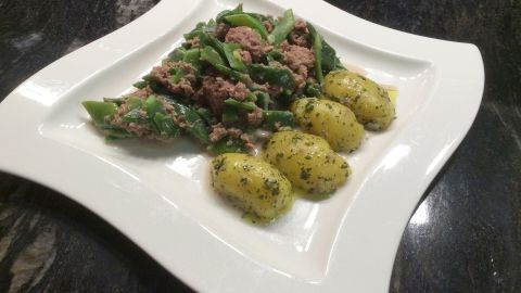 Ein Teller mit grünen Bohnen und Corned Beef liegt auf einer eleganten weißen Servierplatte neben Kartoffeln in Kräutersauce.