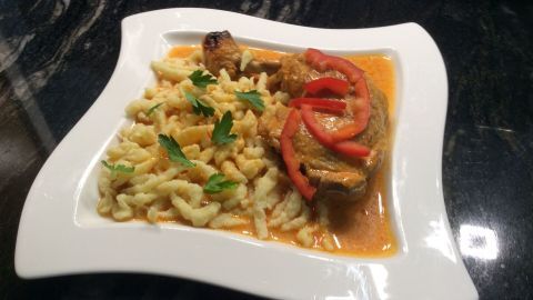 Ein köstliches Paprikahühnchen mit Sauce und frischen Tomatenscheiben, serviert auf einem Teller mit Spätzle.