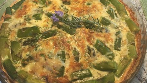 Eine Tarte mit grünem Spargel liegt auf einem dekorativen Tischläufer, umgeben von einem Getränk im Hintergrund.