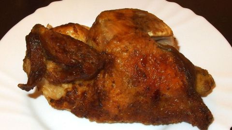 Ein saftiges Brath&auml;hnchen liegt auf einem wei&szlig;en Teller, perfekt gegart und goldbraun, bereit zum Servieren.