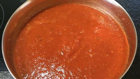 Eine große Schüssel mit frischem Tomatenbelag steht auf einer schwarzen Arbeitsfläche, bereit für die perfekte Pizza.