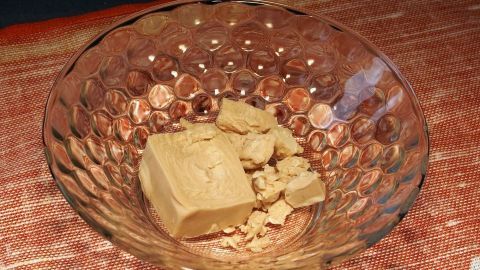 Hefereste, aufgelöst in Wasser, als Blumendünger verwenden. Ein Stück Hefe liegt in einer gläsernen Schüssel auf einem Tisch, bereit zur Verwendung als Blumendünger in Pflanzenpflege.
