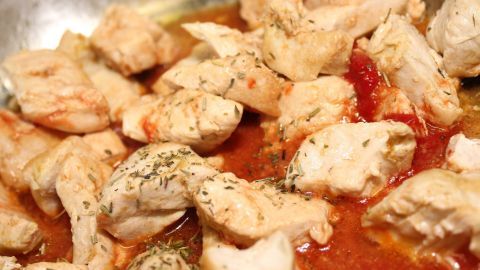 Zarte Hühner- oder Putengeschnetzeltes wird in einer Pfanne mit einer würzigen Sauce zubereitet, umgeben von frischen Kräutern.