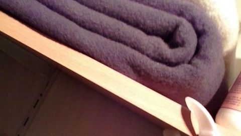 Faltige Wolldecken liegen ordentlich auf einem Regal, während ein Aufhänger in einem Schrank zur Aufbewahrung dient.