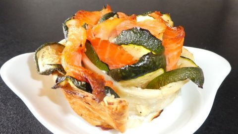 Auf einem weißen Teller liegt eine Blätterteig-Blume, gefüllt mit Lachs und Zucchini, angerichtet auf einer dunklen Tischoberfläche.