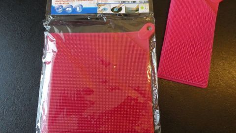 Ein roter Silikonschwamm liegt verpackt und daneben unverpackt, ideal für grobe Verschmutzungen an Kochgeschirr.