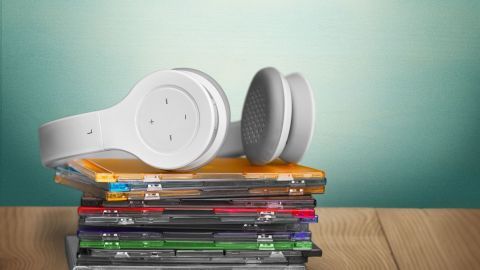 Kopfhörer liegen auf einem Stapel bunter CDs, die auf einem Holztisch platziert sind, mit einem sanften Hintergrund.