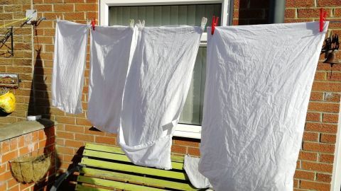 Helle, frisch gewaschene weiße Textilien hängen an einem Wäscheständer vor einem Fenster, um an der Sonne zu trocknen.