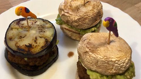 Ein mit frischen Zutaten zubereiteter Low-Carb-Burger ohne Brötchen liegt auf einem Teller, umgeben von einer Holztischoberfläche.