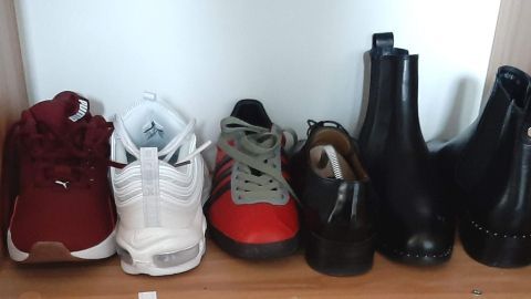 Rote Sneakers, weiße Sportschuhe und schwarze Stiefel stehen ordentlich nebeneinander auf einem Holzregal zur platzsparenden Aufbewahrung.