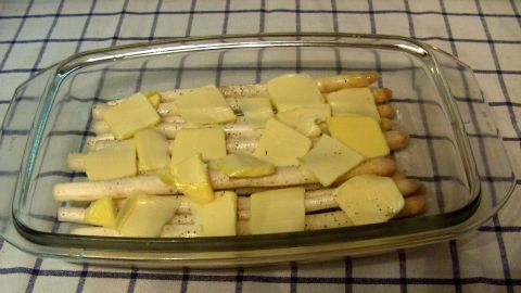 Zarte Spargelstangen liegen in einer Glasauflaufform, bedeckt mit Käse, bereit zum Backen im Ofen.