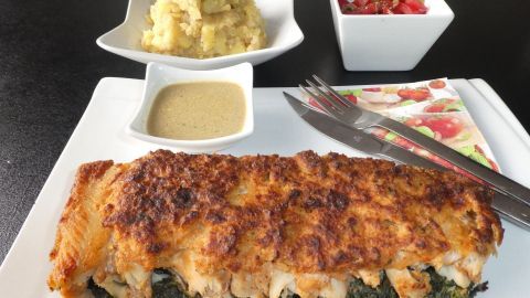 Überbackener Fisch mit knuspriger Kruste liegt auf Blattspinat, serviert mit Beilagen in kleinen Schalen.