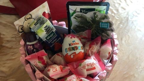 Ein herzförmiger Korb ist gefüllt mit Süßigkeiten und kleinen Geschenken auf einem Holztisch, ideal für eine selbst gebastelte Geschenkidee.