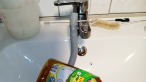 Ein Flasche Reinigungsmittel steht neben einem Waschbecken, während der Abflussschlauch zu reinigen versucht wird.