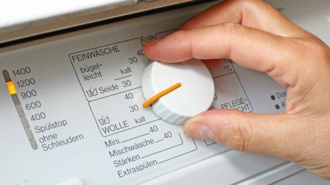 Ein Hand mit einem Drehknopf an einer Waschmaschine stellt das Programm für die Wäsche ein, um echte Wolle richtig zu waschen.