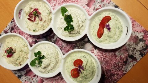 Sechs Schalen mit Kräuterquark sind schön angerichtet, jede mit verschiedenen frischen Kräutern und Gemüse dekoriert.