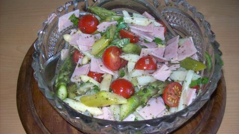 Ein bunter Salat aus grünem und weißem Spargel mit Tomaten und Gurken in einer Schüssel auf einem Holzbrett.