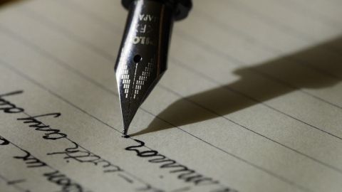 Eine Federkiel schreibt in fließender Schrift auf ein liniertes Blatt Papier, umgeben von einem ruhigen, kreativen Ambiente.