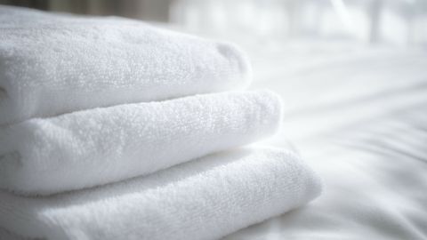 Weiche, weiße Handtücher liegen ordentlich gestapelt auf einem Bett, umgeben von heller, sanfter Tageslichtatmosphäre.