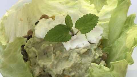 Eine große Salatblatt-Schale hält eine cremige Mischung aus Kidneybohnen und Kichererbsen, dekoriert mit Minze.