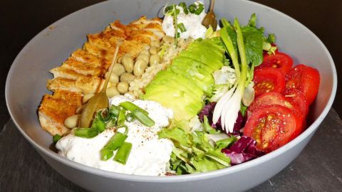 Ein Salat mit Hähnchenbrust liegt in einer grauen Schüssel, bunt angereichert mit frischem Gemüse und Dressing.