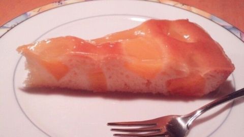 Eine saftige Pfirsich-Joghurt-Tarte liegt auf einem Teller, angelehnt an eine Gabel, umgeben von einem holzigen Tisch.